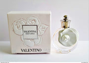 A miniature bottle of Valentino Valentina Acqua Floreale Eau De Toilette is placed next to its white embossed box, both featuring a floral design, highlighting this exquisite fragrance for women from Valentino.