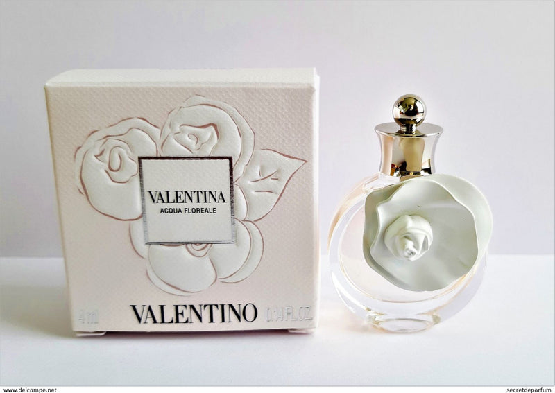 Load image into Gallery viewer, A miniature bottle of Valentino Valentina Acqua Floreale Eau De Toilette is placed next to its white embossed box, both featuring a floral design, highlighting this exquisite fragrance for women from Valentino.
