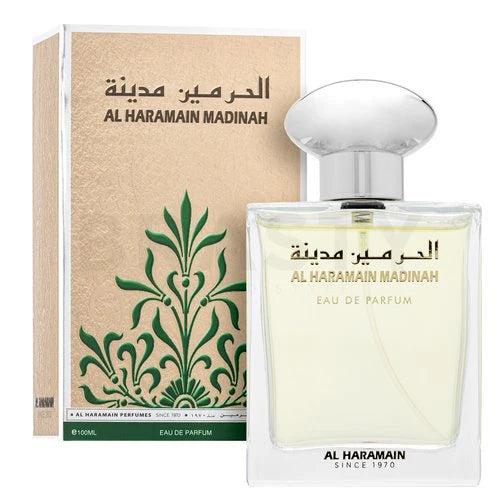 The image shows a box and a 15ml glass bottle of "Al Haramain Madinah Pure Perfume 15ml" by Al Haramain. The box is beige with green floral designs, while the clear bottle features a round silver cap and matching label text.