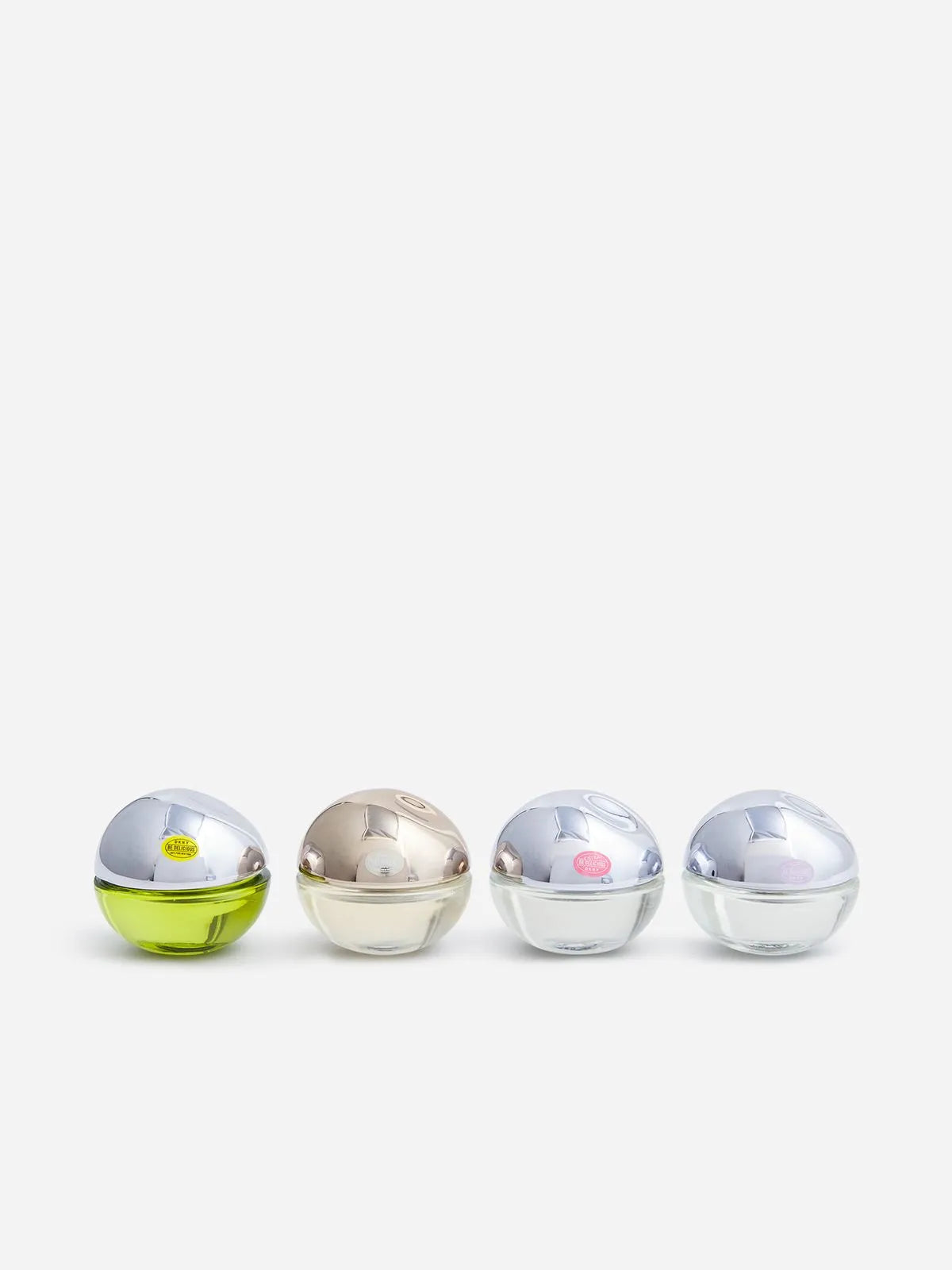 A chic mini set of four spherical DKNY bottles, each topped with metallic caps, is arranged in a row. The first bottle contains a green liquid that evokes the essence of DKNY Be Delicious Eau de Parfum, followed by clear liquid in the other elegant bottles.