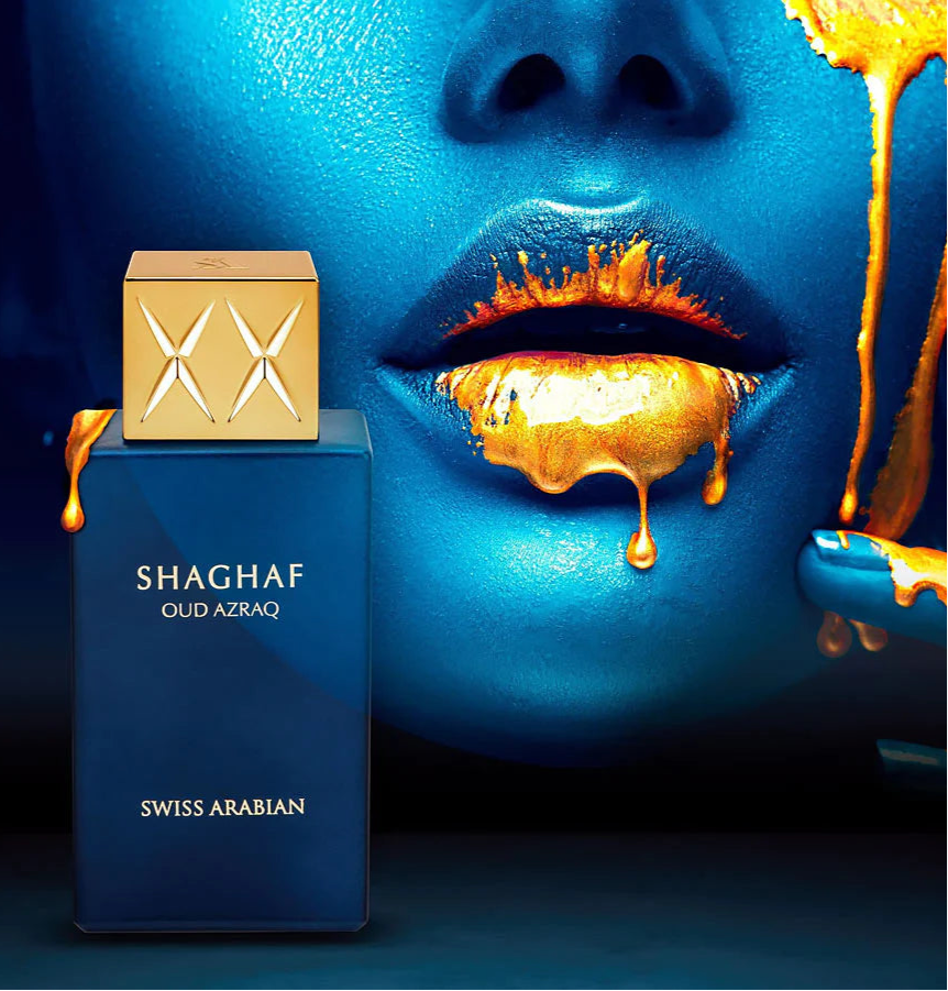 A blue face with golden lips looks at a gold-capped blue bottle of Swiss Arabian Shaghaf Oud Azraq Limited Edition 75ml Eau De Parfum, enticingly labeled to offer an amber woody fragrance.