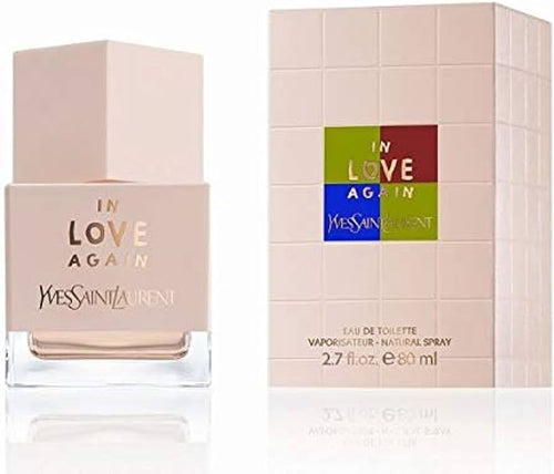 A bottle of YSL La Collection In Love Again 80ml Eau De Toilette stands next to its matching box, featuring a pink and multicolored design with the Yves Saint Laurent brand name and perfume logo, capturing the essence of a floral fruity fragrance.