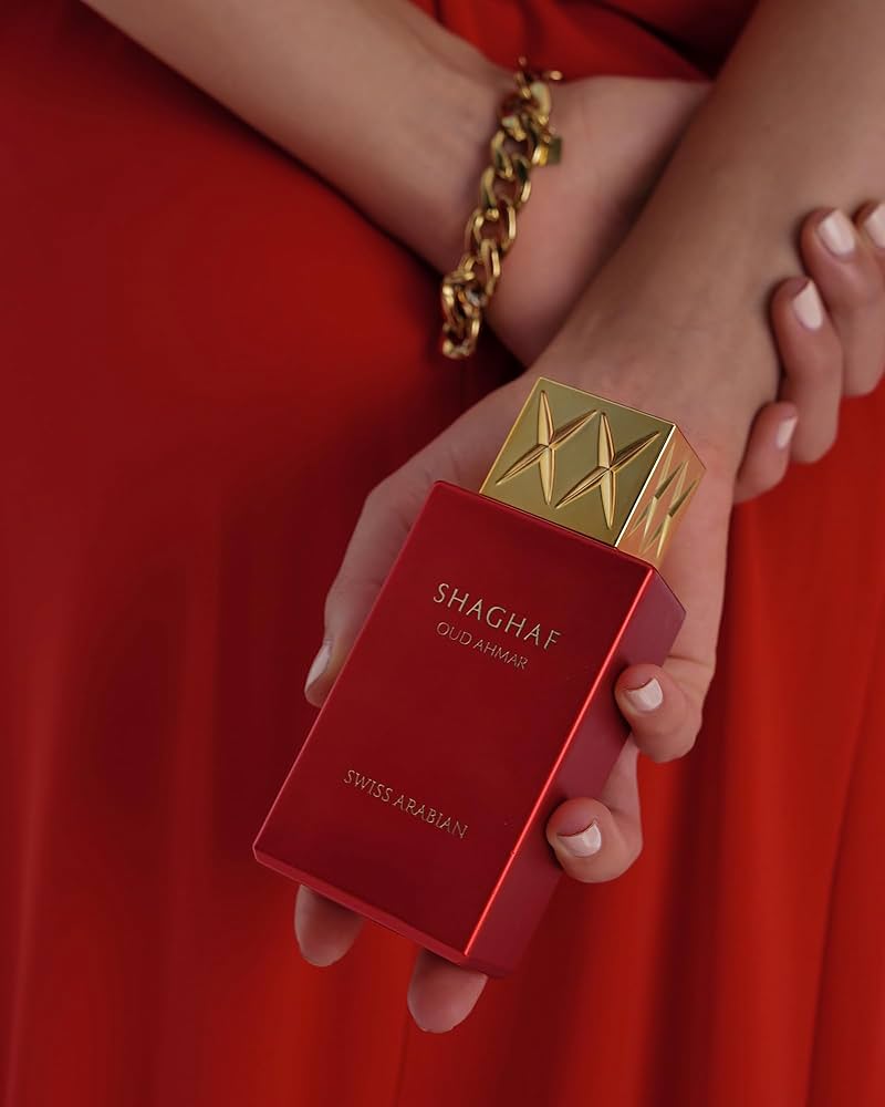 A woman in a red dress holding a Swiss Arabian Oud Ahmar 75ml Eau De Parfum bottle, exuding the captivating fragrance of this Swiss Arabian.