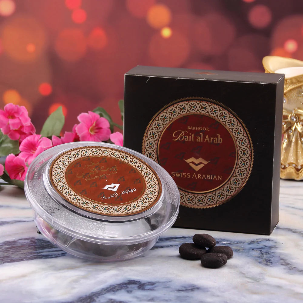 A box of Swiss Arabian Bakhoor Bait Al Arab Bukhoor, part of a Buy 1 Get 1 Free promotion, lies beside a sleek black case. The ScentStory brand's oud fragrance wafts through pink flowers against an ornate backdrop, creating an enchanting scene.