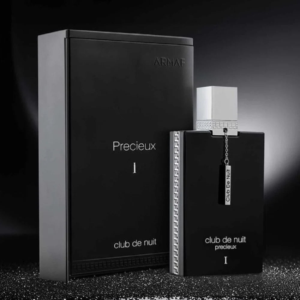 A stylish, black Armaf Club de Nuit Precieux Extrait De Parfum bottle is gracefully positioned beside its matching box on a dark, textured surface. This Oriental Woody fragrance delivers an enticing mix of mystery and elegance.