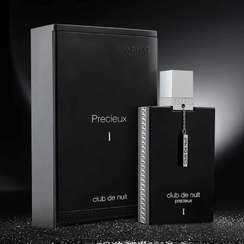 Load image into Gallery viewer, A stylish, black Armaf Club de Nuit Precieux Extrait De Parfum bottle is gracefully positioned beside its matching box on a dark, textured surface. This Oriental Woody fragrance delivers an enticing mix of mystery and elegance.
