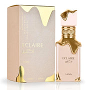 The Lattafa Eclaire 100ml Eau De Parfum showcases a gold-themed bottle beside its matching box, adorned with floral fruity gourmand notes. With gold accents and bilingual English and Arabic text, this exquisite item reflects Lattafa's artistry.