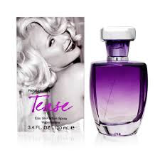 A Paris Hilton Tease 100ml EDP perfume bottle, with its distinct purple hue and "Tease" label, is placed next to its accompanying box featuring a black and white photo of a smiling woman with curly blonde hair, reminiscent of Marilyn Monroe.