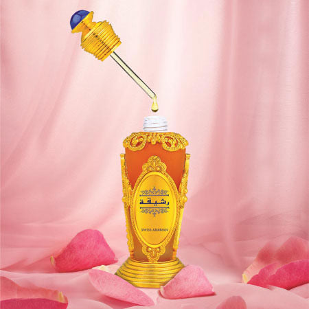 Load image into Gallery viewer, A decorative perfume bottle featuring a gold and blue dropper, highlighting Swiss Arabian Rasheeqa 20ml Concentrated Perfume Oil, is nestled among pink rose petals on a pink backdrop, exuding an enchanting floral aroma.
