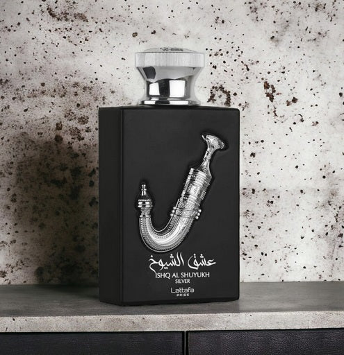 A Lattafa Ishq Al Shuyukh Silver 100ml Eau De Parfum bottle, featuring a black design with silver decorative elements, is elegantly placed against a speckled stone background.