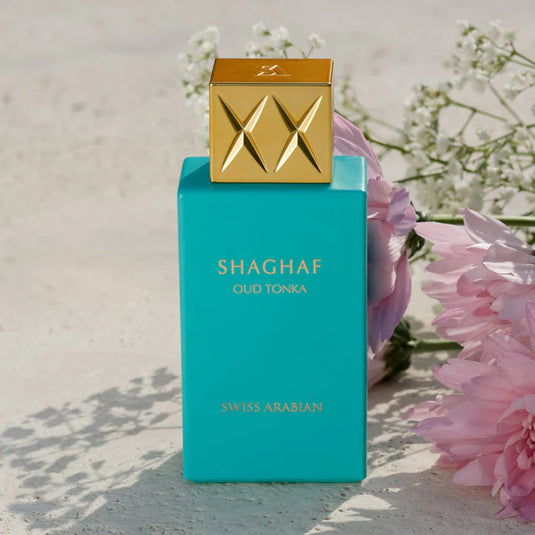 A teal perfume bottle labeled "Swiss Arabian Oud Tonka 75ml Eau De Parfum" by Rio Perfumes, adorned with a golden cap and set against a backdrop of floral decorations. This Eau De Parfum is a captivating fragrance that exudes elegance and charm.