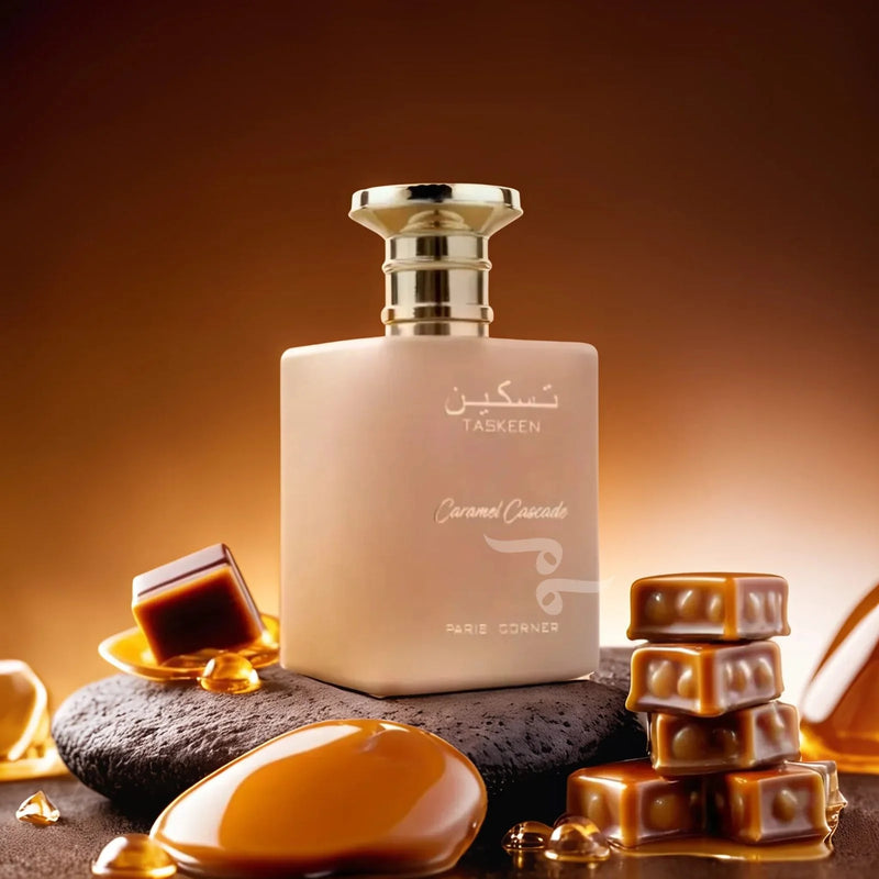 Load image into Gallery viewer, A frosted perfume bottle labeled &quot;Paris Corner Taskeen Caramel Cascade,&quot; surrounded by caramel pieces, displayed on a dark stone with a warm, brown background. This floral fruity gourmand fragrance is an indulgent treat for the senses.
