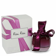 A 50ml bottle of Ricci Ricci by Nina Ricci Eau De Parfum, featuring a purple bow cap, is positioned next to its box, which is intricately decorated with a matching purple ribbon design.