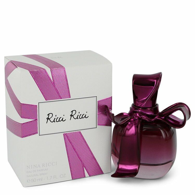 Load image into Gallery viewer, A 50ml bottle of Ricci Ricci by Nina Ricci Eau De Parfum, featuring a purple bow cap, is positioned next to its box, which is intricately decorated with a matching purple ribbon design.
