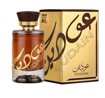 A bottle of Rio Perfumes Lattafa Oudain 100ml Eau De Parfum with a brown wooden cap, placed next to its golden box adorned with Arabic script and "OUDAIN" text. This exquisite fragrance for men exudes elegance and luxury.