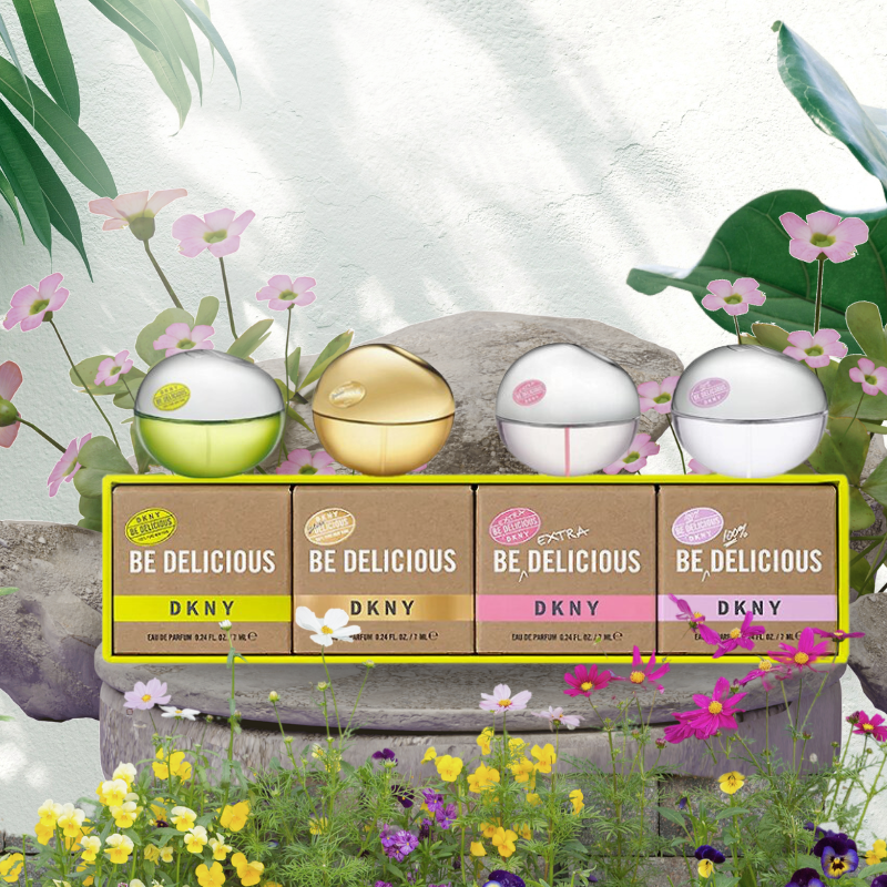 Load image into Gallery viewer, A set of four DKNY Be Delicious Eau de Parfum miniatures is artfully arranged on a stone surface outdoors, surrounded by vibrant flowers and lush greenery.
