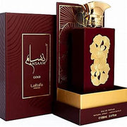 Maroon and gold perfume bottle with floral design on label, placed next to its matching box. Label reads "Lattafa Ansaam Gold 100ml Eau De Parfum" by Lataffa. The box has Arabic script, hinting at an Amber Floral fragrance, and the bottle is 100ml.