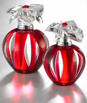 Two bottles of Cartier Delices 100ml EDT, featuring a red apple-shaped design and translucent flower-like caps, are displayed on a reflective surface. They cast a soft glow while exuding a luxurious aroma reminiscent of an original Cartier fragrance.