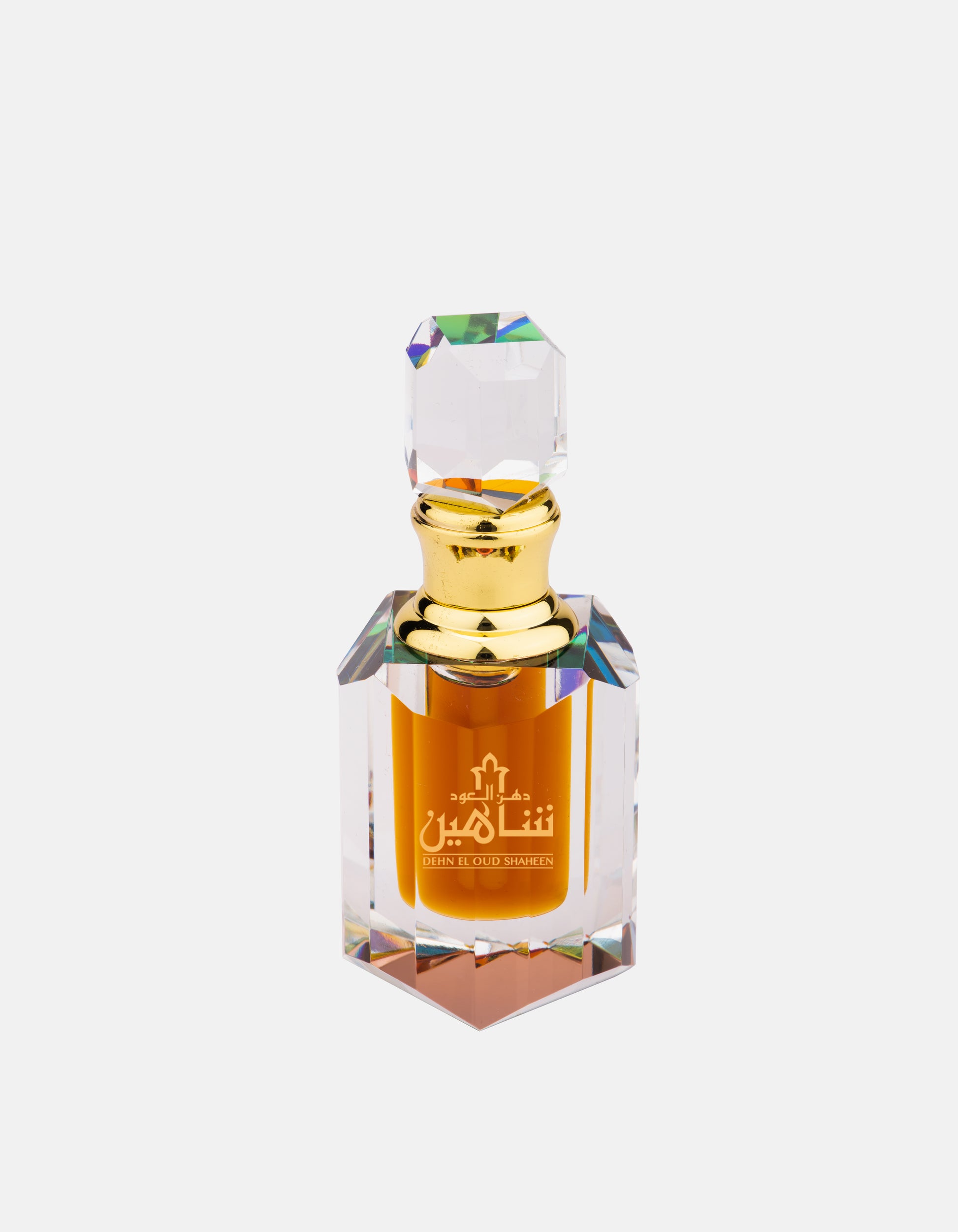 A bottle of Swiss Arabian Dehn El Oud Shaheen concentrated oil with a golden cap and a transparent, faceted glass design, filled with amber liquid, captures the essence of a luxurious unisex concentrated perfume oil.