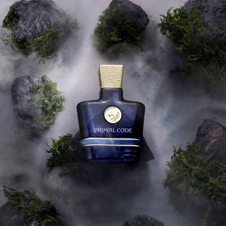 A dark blue Eau De Parfum bottle labeled "Swiss Arabian Primal Code 100ml Eau De Parfum" is surrounded by rocks and green moss, with mist in the background—a true fragrance for men by Swiss Arabian.