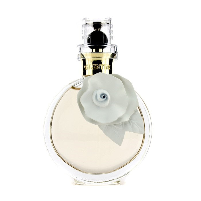 The Valentino Valentina Acqua Floreale miniature Eau De Toilette by Valentino is a clear round perfume bottle adorned with a large white flower ornament on the front and topped with a transparent cap. Inside, the pale yellow liquid offers an exquisite fragrance for women.